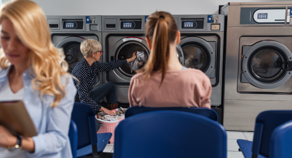 three women in laundry mat washing clothes and reading magazines