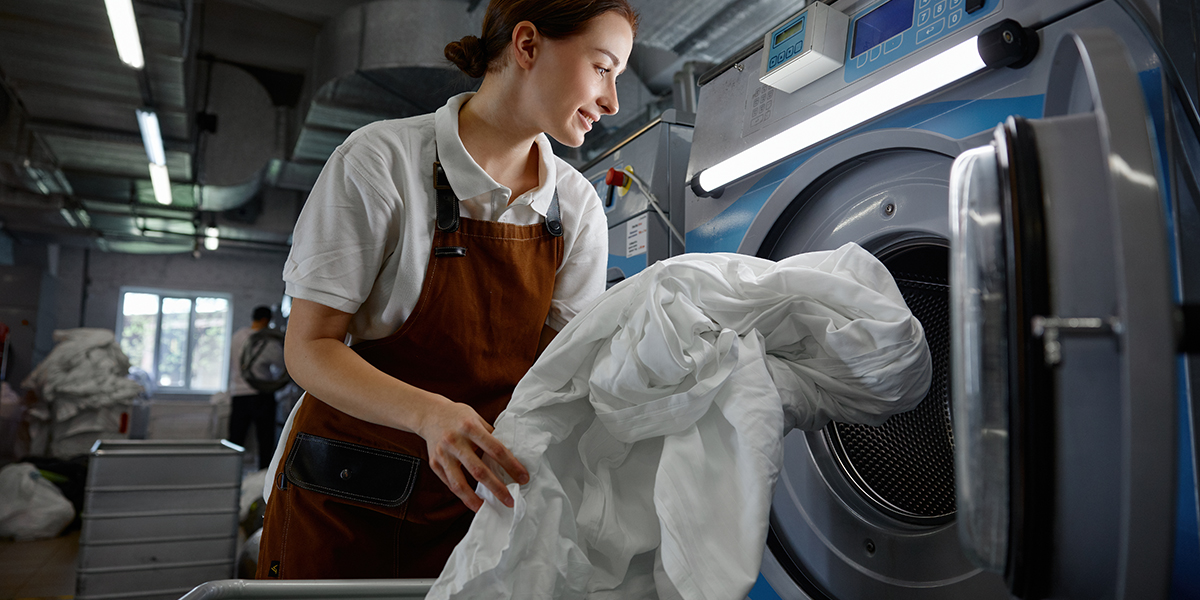 A woman is in the process of putting various clothes into a washing machine
